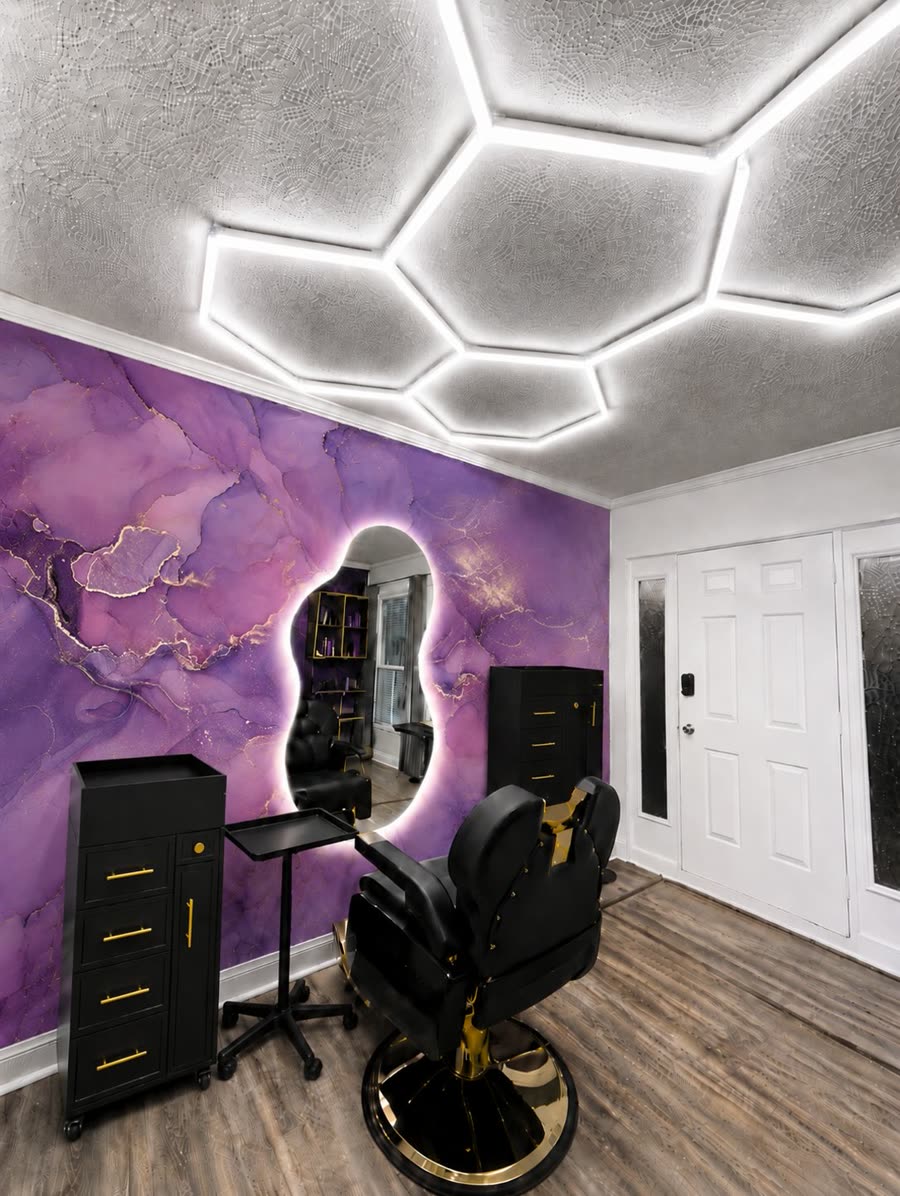 Interior del estudio: pared de mármol lila con vetas doradas, espejo con luz halo y silla negra con base dorada.